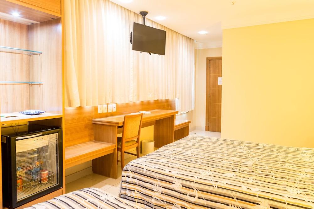 Hotel Atlântico Business Centro Rio de Janeiro Esterno foto The photo shows a hotel room with two beds featuring striped bedding. There is a wooden desk and chair near a window with light-colored curtains. A flat-screen television is mounted on the wall, and there appears to be a small refrigerator or mini-ba